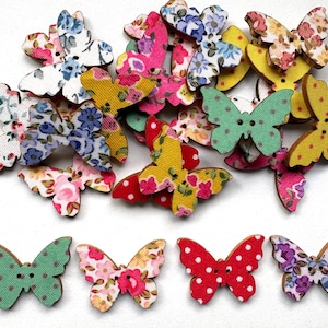 May include: A collection of wooden butterfly-shaped buttons in various colors and patterns. The buttons feature floral, polka dot, and solid designs in shades of pink, yellow, blue, and green. Each button has two small holes for sewing.
