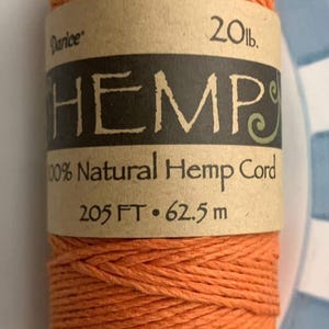 May include: Orange hemp cord spool with a label that reads "HEMP 100% Natural Hemp Cord 205 FT • 62.5 m". The label also indicates the spool contains 20 lbs of cord. The cord is a vibrant orange color.