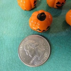 May include: A close-up of four orange and black Halloween pumpkin-shaped ornaments. The ornaments are about the size of a US quarter.