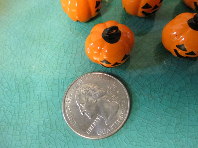 May include: A close-up of four orange and black Halloween pumpkin-shaped ornaments. The ornaments are about the size of a US quarter.