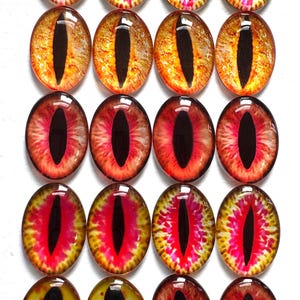 May include: A collection of twenty oval-shaped glass eye cabochons. The eyes feature a black vertical slit pupil, surrounded by vibrant colors including red, yellow, and orange, creating a striking, detailed design. These are suitable for crafting.
