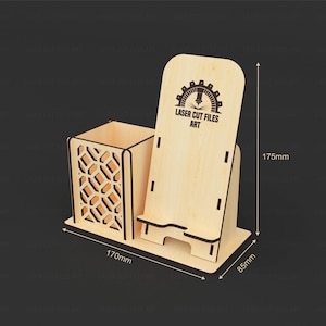 May include: A light-colored wooden desk organizer featuring a square pen holder with a geometric cutout pattern and an integrated phone stand. The stand displays the text LASER CUT FILES ART. Dimensions are 170mm wide, 85mm deep, and 175mm high.