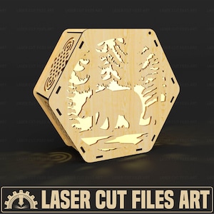 May include: A wooden, hexagonal box with laser-cut designs. The front panel features a bear in a forest scene. The box is made of light-coloured wood. The text "LASER CUT FILES ART" is at the bottom.