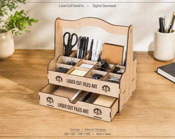 May include: A light-colored wooden desk organizer with a handle, multiple upper compartments, and a bottom drawer. The front of the unit features the text Laser Cut Files Art. The organizer holds various office supplies including scissors, pens, and clips.