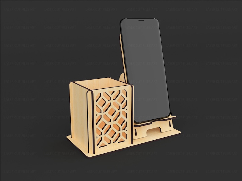 May include: A light-colored wooden desk organizer featuring a square pen holder with a geometric cutout pattern on the side and an integrated upright stand designed to hold a smartphone in a vertical position on a flat rectangular base.