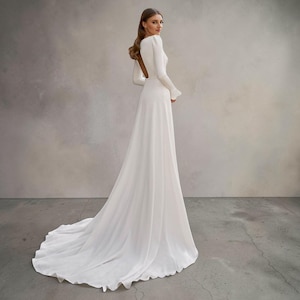 May include: A white wedding dress with a long train and sleeves. The dress has a high neckline and a fitted bodice that flows into a full skirt. The sleeves have a slight bell shape at the wrist. The background is a neutral grey.