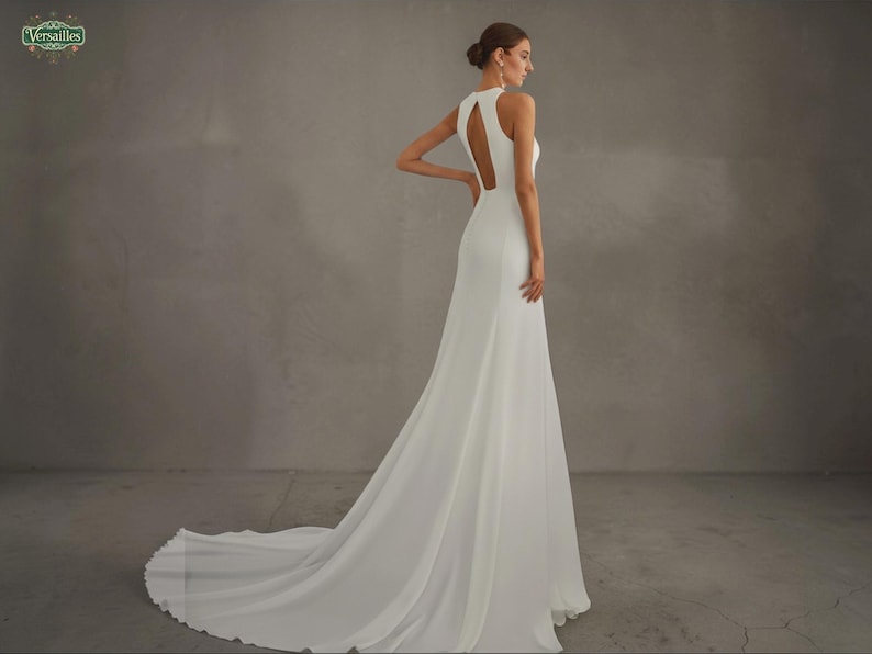May include: A white wedding dress with a halter neckline and a flowing skirt. The dress features a keyhole back and a long train. The image is set against a neutral gray background. The Versailles logo is in the top left corner.