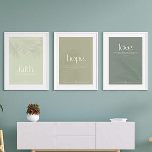 Könnte beinhalten: Drei gerahmte Wandbilder mit den Wörtern faith, hope und love in weißer Serifenschrift auf salbeigrünen Hintergründen mit dezenten Palmblattmustern, präsentiert in weißen Rahmen über einem weißen Sideboard-Schrank.