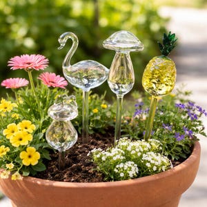 May include: A terracotta pot filled with colorful flowers and decorative glass garden stakes. The stakes are shaped like a swan, mushroom, pineapple, and another mushroom. The pineapple stake is yellow and green, while the others are clear glass.