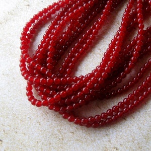 May include: A strand of red gemstone beads. The beads are round and smooth, and they are strung on a clear thread.
