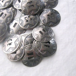 May include: A pile of silver-toned metal star-shaped conchos with a textured surface. Each concho has three rectangular cutouts in the center.
