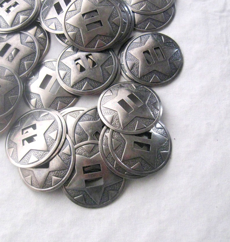 May include: A pile of silver-toned metal star-shaped conchos with a textured surface. Each concho has three rectangular cutouts in the center.