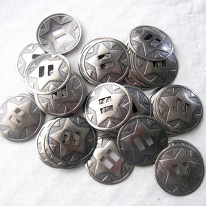 May include: A pile of silver-toned metal conchos with a star design and two slits. The conchos are approximately 1 inch in diameter.