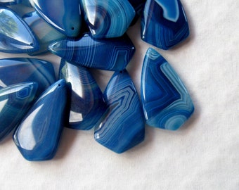 May include: A group of blue agate gemstone pendants with white banding. The pendants are shaped like a teardrop with a pointed tip.