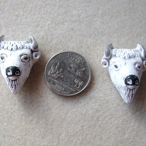 May include: Two white ceramic buffalo head figurines with black noses and gray horns. The figurines are about the size of a US quarter.