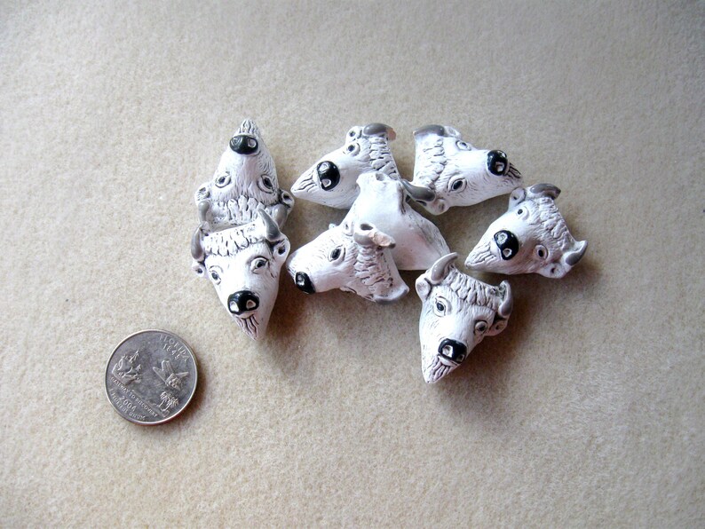 May include: Seven white ceramic buffalo head charms with black eyes and noses. The charms are about the size of a US quarter.