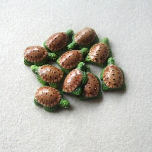 May include: A collection of small, decorative turtle figurines. Each turtle has a green body and a brown shell with a detailed pattern. The figurines are arranged closely together, creating a clustered display.