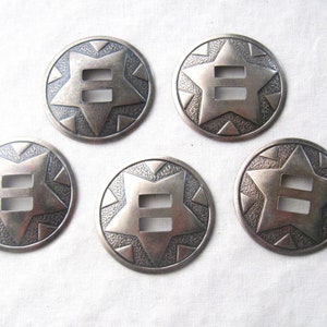 May include: Six silver-toned metal conchos with a star design and a double-slot opening. The conchos have a textured surface and are perfect for adding a western touch to your projects.