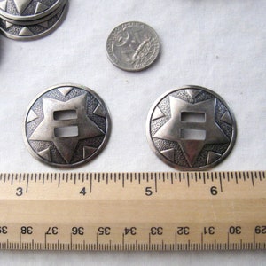 May include: Two silver-toned metal conchos with a starburst design and a double-slot opening. The conchos are approximately 1.75 inches in diameter.