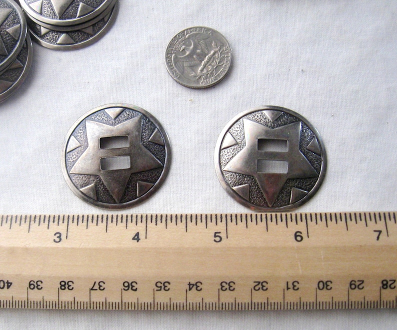 May include: Two silver-toned metal conchos with a starburst design and a double-slot opening. The conchos are approximately 1.75 inches in diameter.