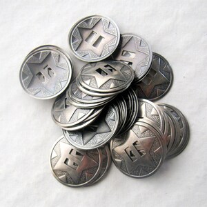 May include: A pile of silver-toned metal buttons with a star design and numbers on them. The buttons are stacked on top of each other and have a textured surface.