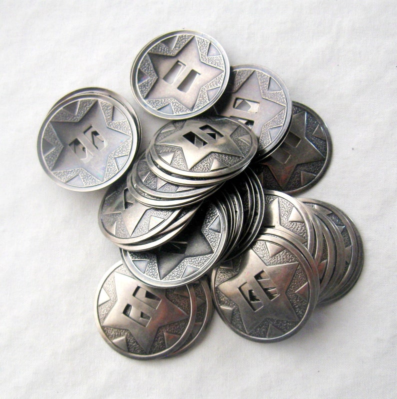 May include: A pile of silver-toned metal buttons with a star design and numbers on them. The buttons are stacked on top of each other and have a textured surface.