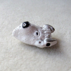 May include: White ceramic animal figurine of a wolf with black eyes. The figurine is lying on its side with its head tilted back.