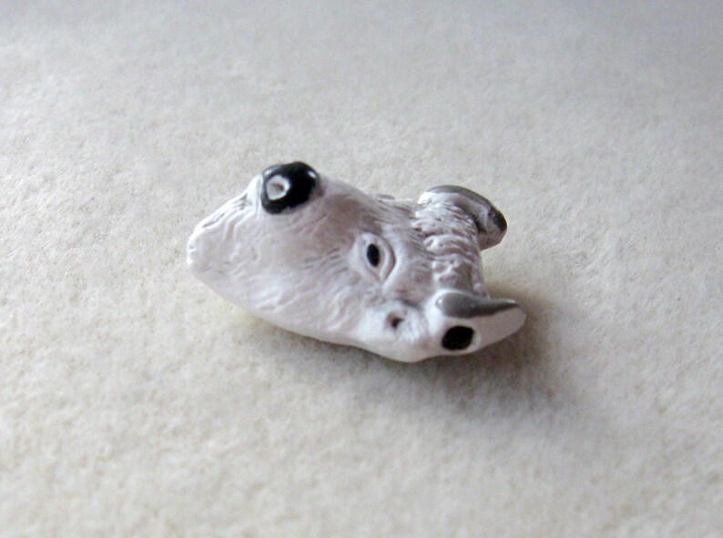 May include: White ceramic animal figurine of a wolf with black eyes. The figurine is lying on its side with its head tilted back.