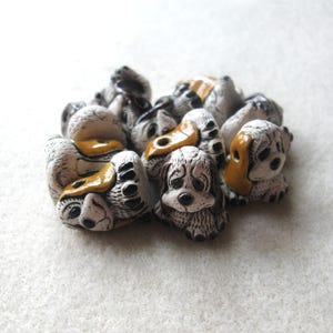 May include: A cluster of small, ceramic dog figurines. The dogs are primarily white with black markings and accents of tan and brown. The dogs are in various poses, some lying down, others sitting.