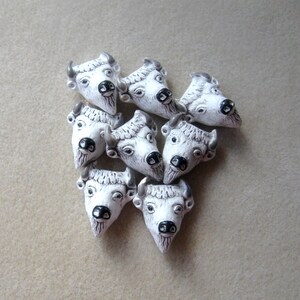 May include: Eight white ceramic buffalo head beads with black eyes and nostrils. The beads are arranged in a heart shape.