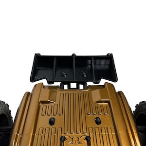 May include: A metallic bronze toy vehicle body featuring a rectangular black rear spoiler. The top surface of the vehicle displays a series of vertical raised ridges and two small black circular fasteners, with black tires visible on the sides.