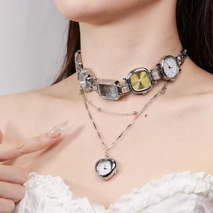May include: A silver-toned necklace featuring a choker-style design with multiple watch faces of various shapes and colors. A heart-shaped pendant with a watch face hangs below. The necklace is a unique fashion accessory.