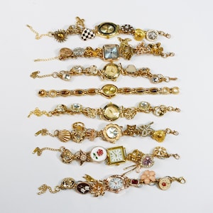 Puede incluir: Una colección de pulseras con dijes doradas con varias esferas de reloj. Las pulseras presentan dijes decorativos, incluyendo soles, flores y formas geométricas. Algunos relojes tienen esferas cuadradas o redondas, y otros tienen números romanos.