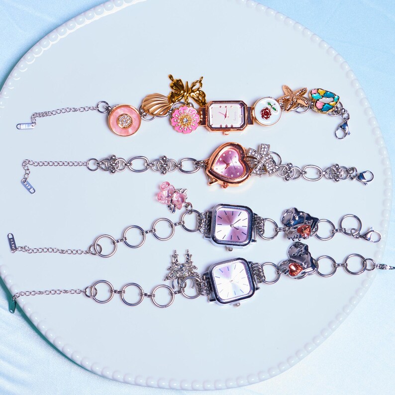 Op de afbeelding: Vier zilveren armbandjes met verschillende wijzerplaten en bedels. De bedels zijn een vlinder, een schelp, een bloem, een hart, een ster en een palmboom.