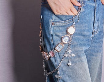 May include: A silver chain with multiple small silver and gold watches attached, hanging from a person's belt loop. The chain also has silver cross charms.