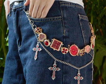 Puede incluir: Un cinturón de cadena plateada con múltiples relojes de esfera roja y tres colgantes de cruz roja. El cinturón está sujeto a unos vaqueros azules. Los relojes tienen diferentes formas, incluyendo redonda, cuadrada y de corazón.