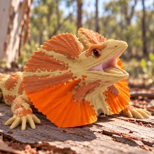 Op de afbeelding: Een kraaghagedis-figuurtje met een getextureerd lichaam met crème en oranje vlekken. De hagedis heeft een uitgespreide, feloranje en crème kraag rond de kop, een geopende bek en een lange, gesegmenteerde staart met bijpassende kleurpatronen.
