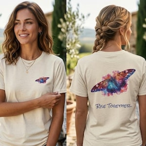 May include: A cream-colored t-shirt featuring a watercolor butterfly design in shades of blue, purple, and red. The text "Rise Together" is printed below the butterfly. The shirt is made of a soft, comfortable material.