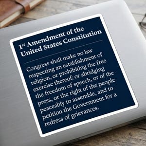 May include: A rectangular sticker with a dark blue background and white text featuring the 1st Amendment of the United States Constitution, which reads: Congress shall make no law respecting an establishment of religion, or prohibiting the free exercise thereof.