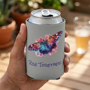 May include: A gray can cooler featuring a colorful butterfly design with blue, purple, and orange hues. The words "Rise Together" are printed in blue below the butterfly. The cooler is designed to keep beverages cold.