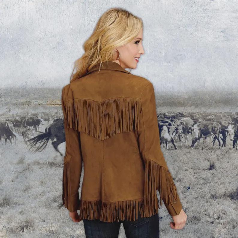 K&ouml;nnte beinhalten: Braune Wildlederjacke mit Fransen am R&uuml;cken, an den &Auml;rmeln und am Saum. Die Jacke hat einen klassischen Western-Stil mit einem Kragen. Der Hintergrund zeigt ein Sepia-Bild einer Rinderherde.