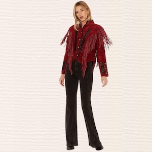 May include: A red suede jacket with fringe detailing and black accents. The jacket has a button-up front and is paired with black flared jeans. The outfit is a western-inspired style.