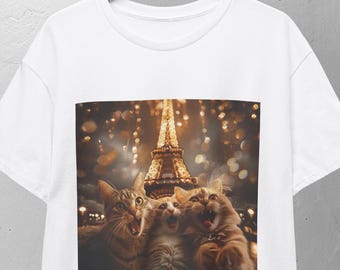 May include: White t-shirt featuring a graphic of three cats in front of the Eiffel Tower at night. The cats appear to be singing or yelling, with the tower illuminated in the background. The shirt is hanging on a wooden hanger.