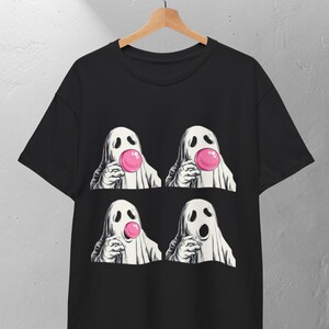 May include: Black t-shirt with a graphic of four cartoon ghosts blowing pink bubble gum bubbles. The ghosts are depicted with white sheets and eye and mouth cutouts. The design is centered on the shirt.