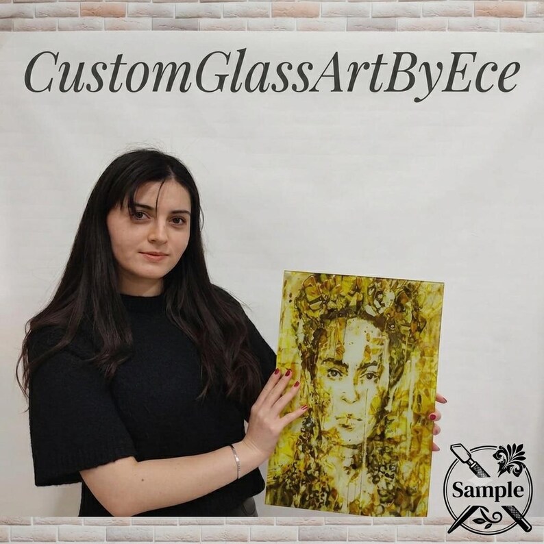 A woman in a black top is holding up a framed artwork of a woman's face, which appears to be a mosaic or collage.