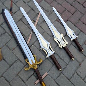 May include: Four fantasy swords with silver blades and gold-colored hilts. The handles are wrapped in brown leather. The swords are arranged on a gray brick surface, with leather straps visible.