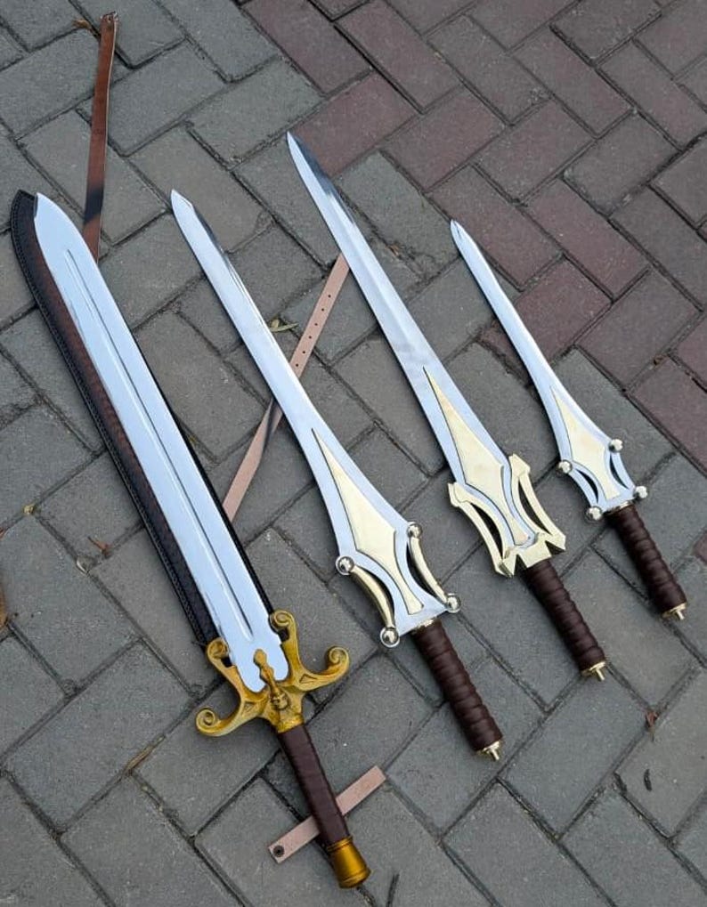 May include: Four swords with silver blades and gold and brown handles are displayed on a brick surface. The swords vary in size, with ornate gold detailing on the hilts and brown leather-wrapped grips. A leather strap is visible.