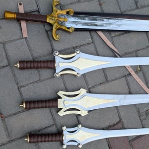 May include: Four decorative swords with ornate gold and silver designs. The swords have brown leather-wrapped handles and detailed gold crossguards. The blades are silver with gold accents. The swords are displayed on a textured surface.
