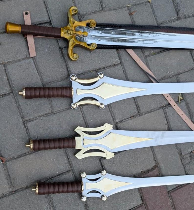 May include: Four decorative swords with ornate gold and silver designs. The swords have brown leather-wrapped handles and detailed gold crossguards. The blades are silver with gold accents. The swords are displayed on a textured surface.