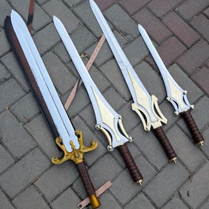 May include: Four decorative swords with silver blades and gold-colored hilts. The handles are wrapped in brown leather. The swords vary in size, with the largest one on the left. The swords are displayed on a gray brick surface.
